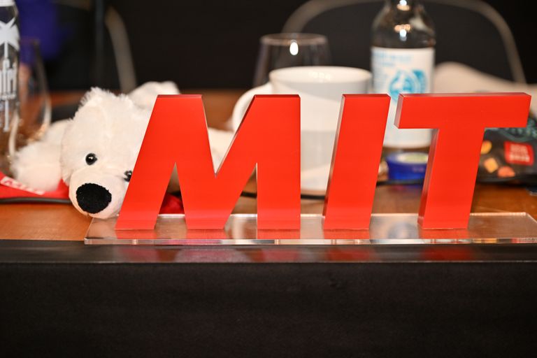 Rotes MIT-Schild auf Tisch mit Stofftier und Bürogegenständen.