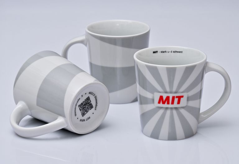 Drei weiße MIT-Mugs mit unterschiedlichen Designs, zwei glatt, einer mit Radialstreifen.